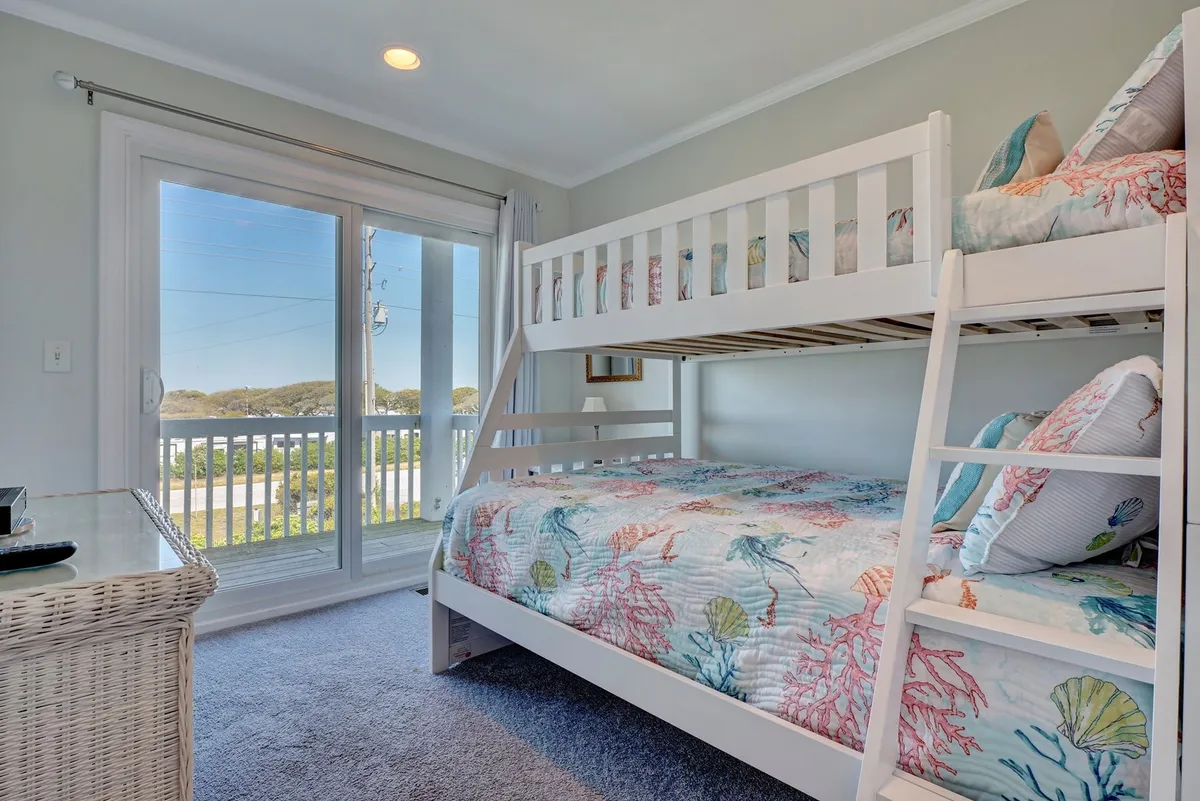 A playful bunk room with a twin-over-full bunk bed dressed in colorful bedding. The room is brightened by ample natural light from a large sliding door, creating a lively yet cozy environment ideal for kids or friends.