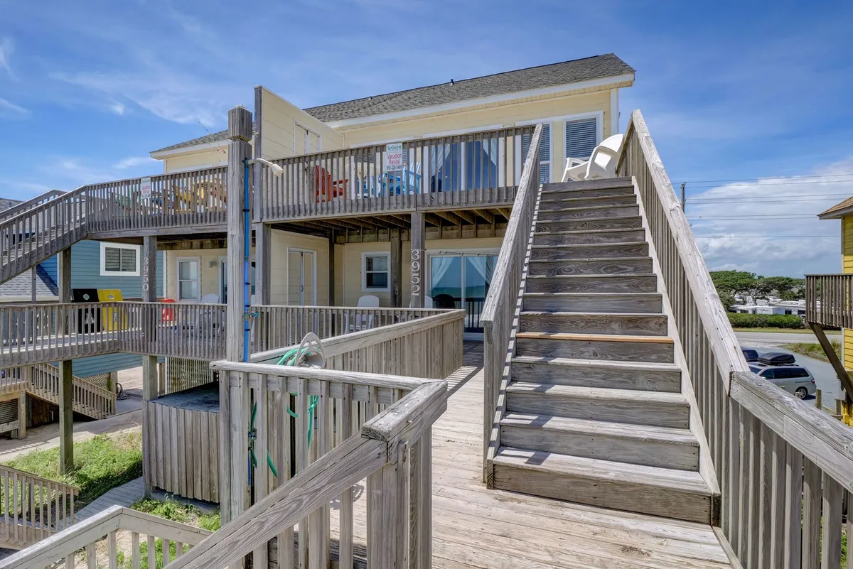 A bright wooden deck with colorful chairs, a staircase leading up, and an open sky above. This exterior shot captures a friendly, social atmosphere ideal for morning coffee, sunset viewing, or alfresco group meals with an ocean breeze.