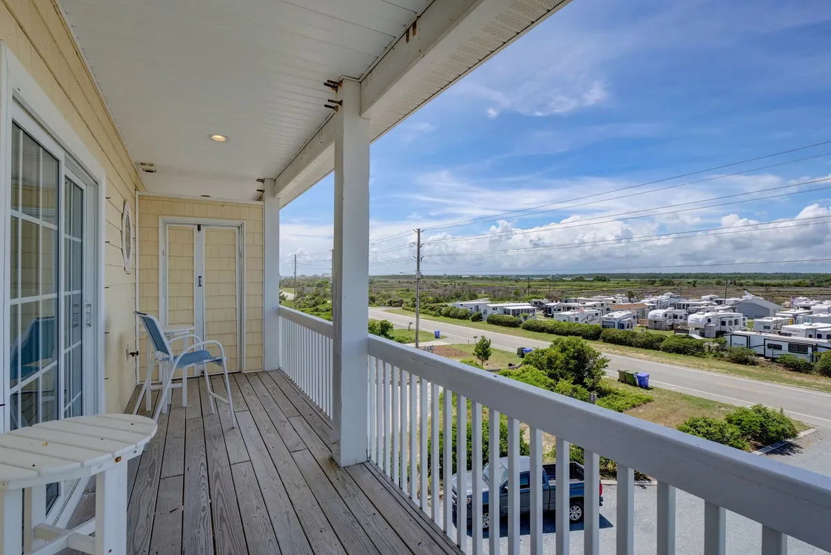 A serene balcony scene featuring a sturdy wooden railing, blue chairs, and a sweeping view of the surrounding landscape. The space feels peaceful yet sociable, perfect for socializing, reading, or savoring drinks together while enjoying the sunset.