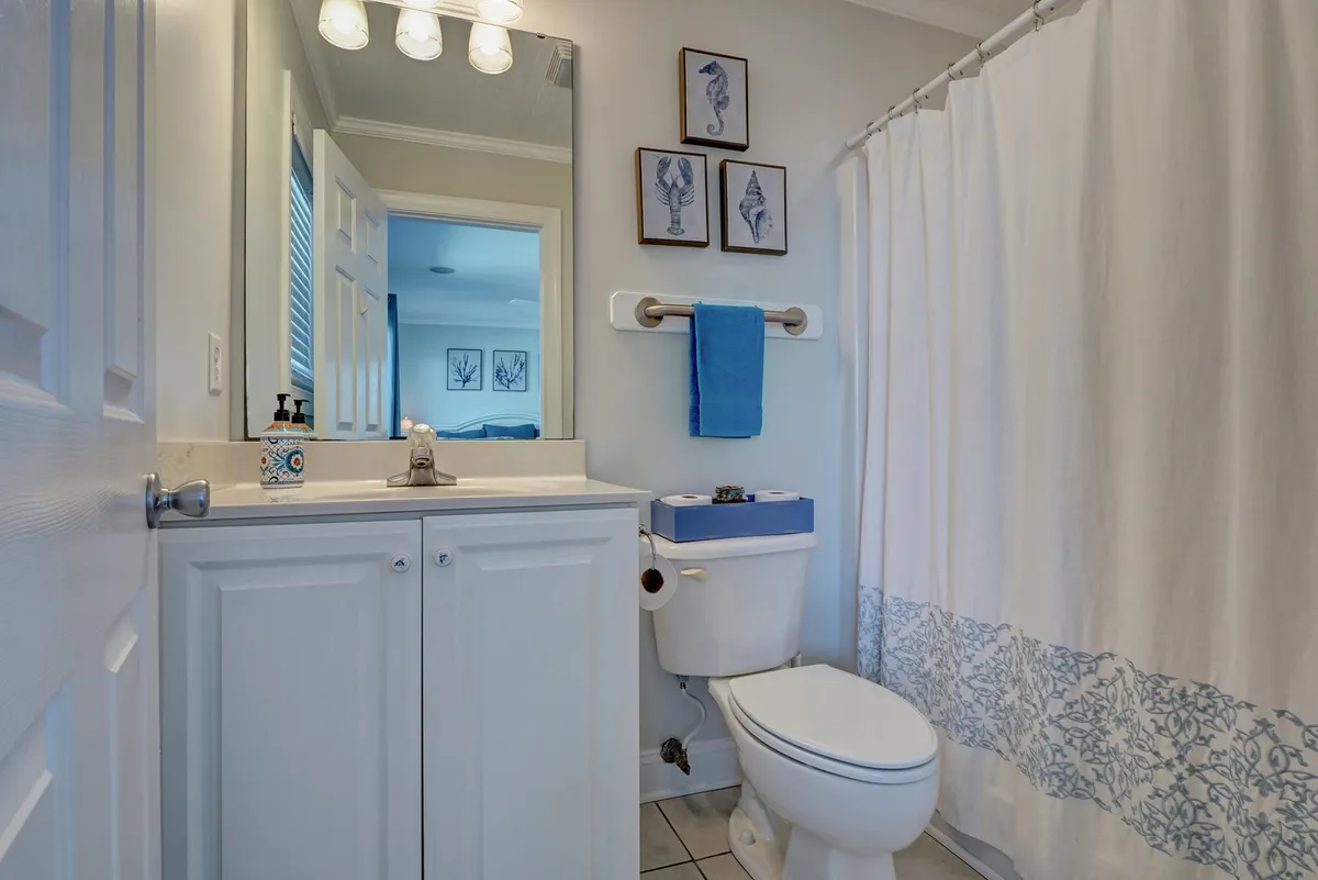 A bright, inviting bathroom with a vanity, sink, and framed sea-themed prints, as well as a shower curtain and tranquil lighting. The space is styled for comfort and relaxation, reinforcing the private bathroom amenity.
