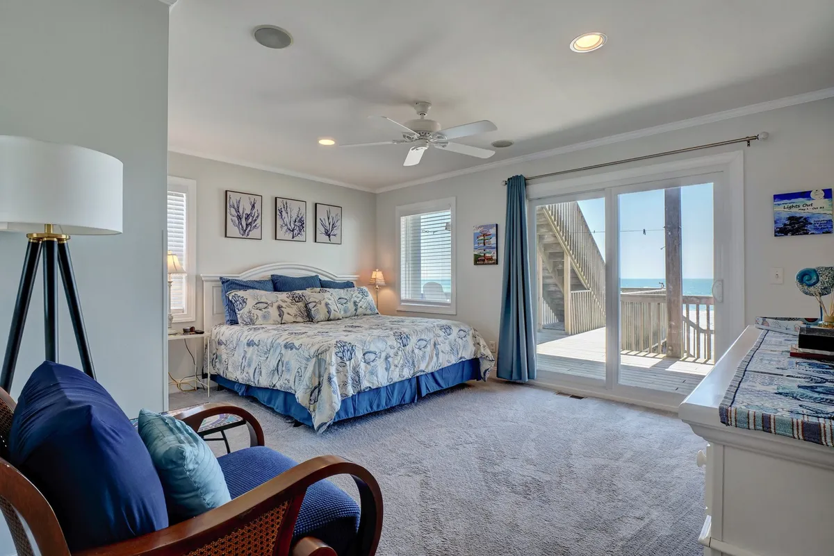 A serene bedroom featuring blue and white bedding, large windows framing the ocean, and coastal accents. The tranquil setting is ideal for relaxing after beach explorations or enjoying quiet moments with the sound of the surf.